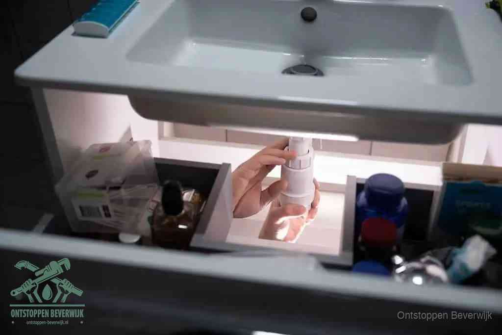 Een pompfles met zeep boven een wastafel, de heet water en afwasmiddel-methode om een vetprop in de afvoer los te maken in Beverwijk