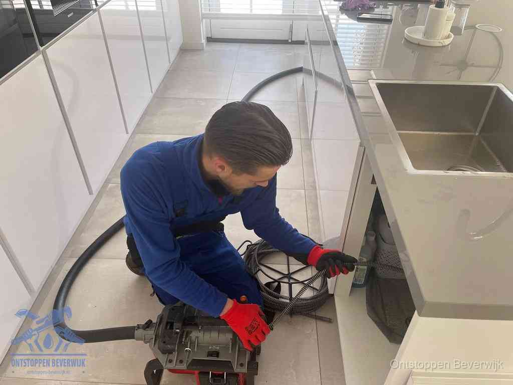 Een monteur ontstopt de keukenafvoer onder de spoelbak met een elektrische veermachine in Beverwijk