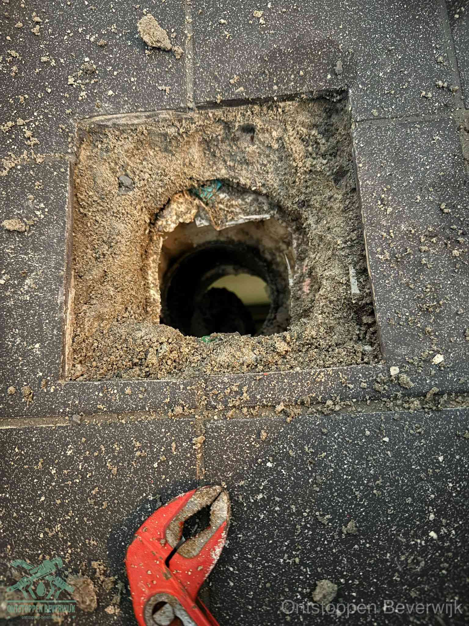 Een geopend rioolputje in een betontegelvloer met losgemaakt rooster en een zichtbare ronde afvoerbuis, het achterhalen waar de afvoerverstopping zit in Beverwijk