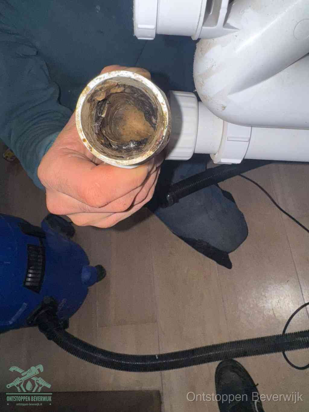 Een hand houdt een losgekoppeld PVC-afvoerbuisstuk vast dat van binnen volledig is dichtgeslibd met vet, vuil en aanslag, de meest voorkomende oorzaak van een verstopte afvoer in Beverwijk