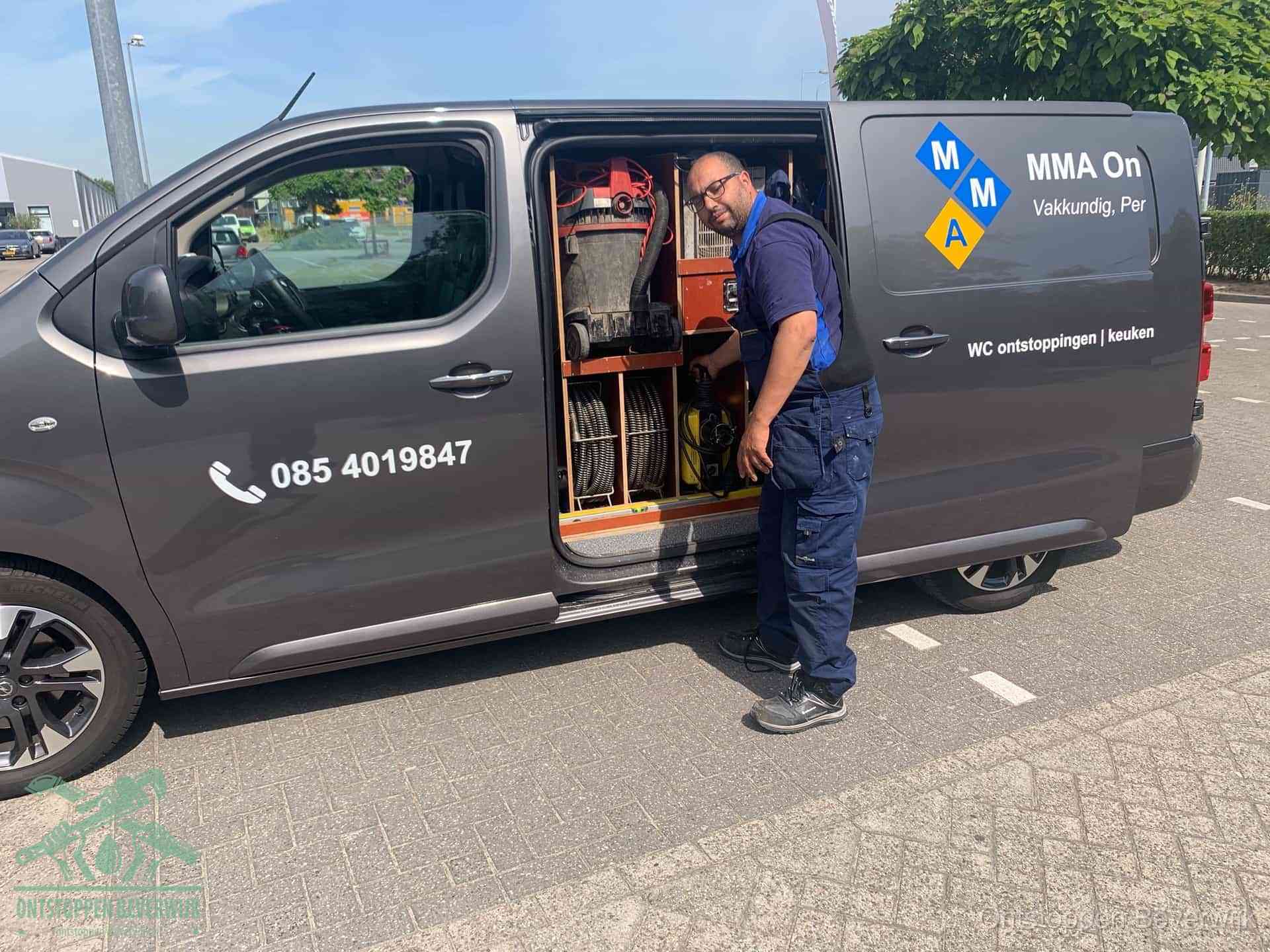 Een monteur bij de open schuifdeur van zijn bedrijfsbus op een parkeerplaats, klaar om de oorzaak van terugkerende afvoerverstoppingen aan te pakken in Beverwijk