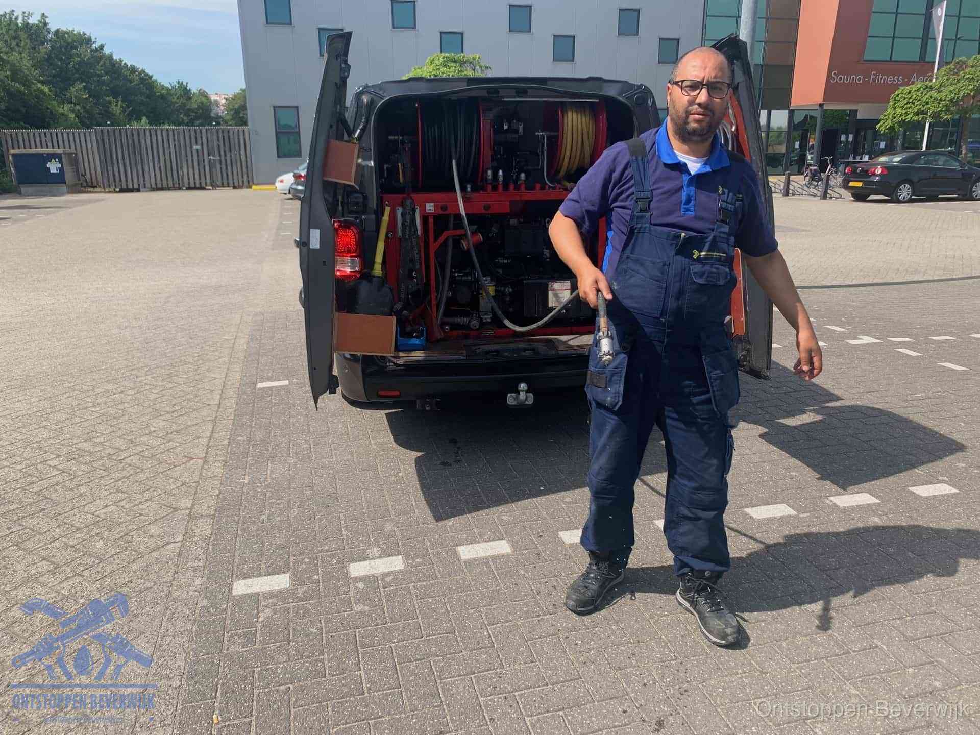 Een monteur bij zijn bestelbus met een hogedruk- en rioolreinigingsunit, klaar om de oorzaak van terugkerende wc-verstoppingen aan te pakken in Beverwijk