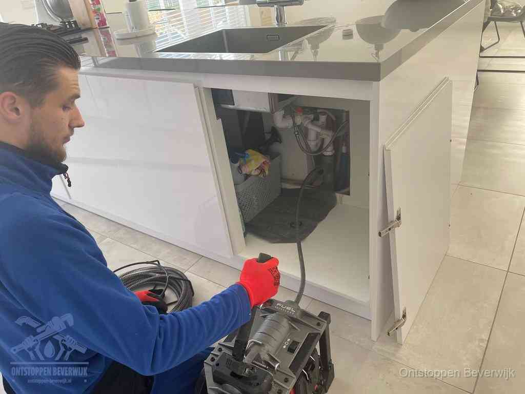 Monteur ontstopt met een veermachine een verstopte afvoer onder de gootsteen in Beverwijk