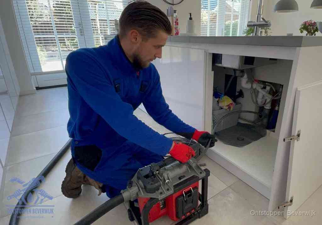 Een monteur voert een professionele elektrische ontstoppingsmachine in de afvoer onder de spoelbak tijdens het gootsteen ontstoppen in Beverwijk