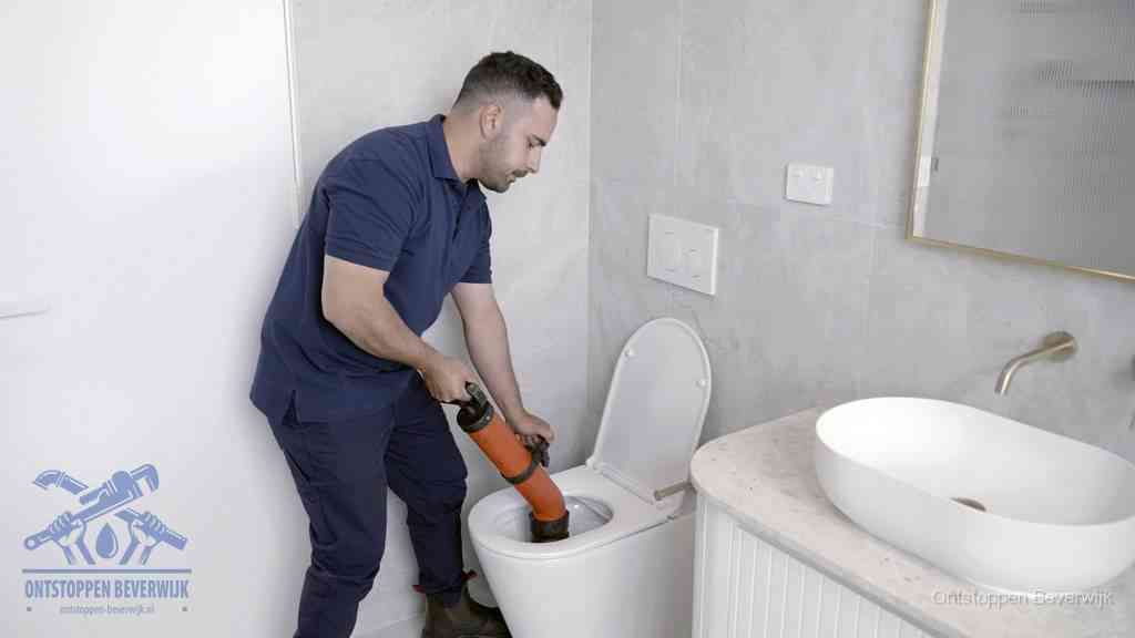 Een man gebruikt een handmatige luchtdruk-ontstopper in een modern betegeld toilet om zelf de wc te ontstoppen in Beverwijk